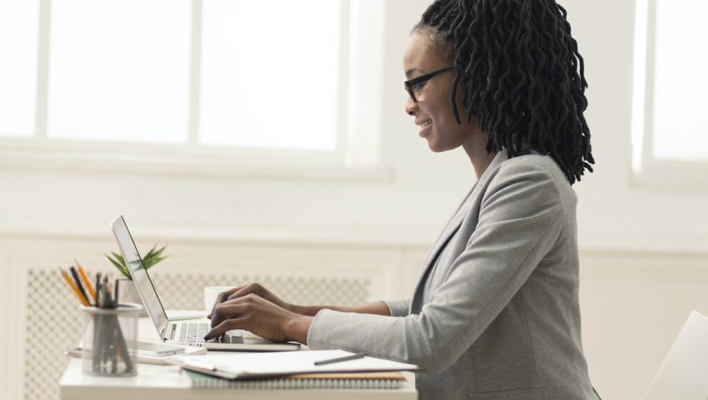 Dame afro-américaine utilisant un ordinateur portable au bureau, vue latérale, panorama