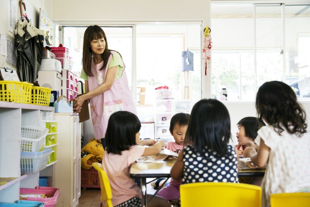 A young woman teacher and group of children in a Japanese preschool seated at a table.