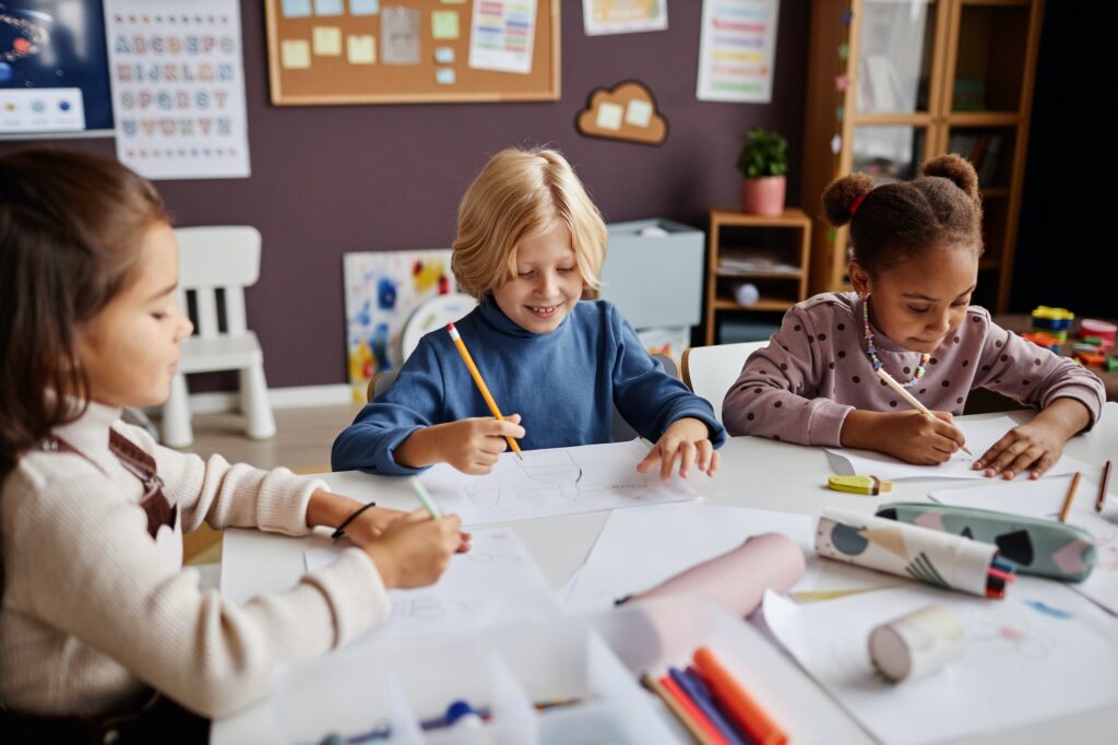 Several diligent learners of nursery school drawing with crayons