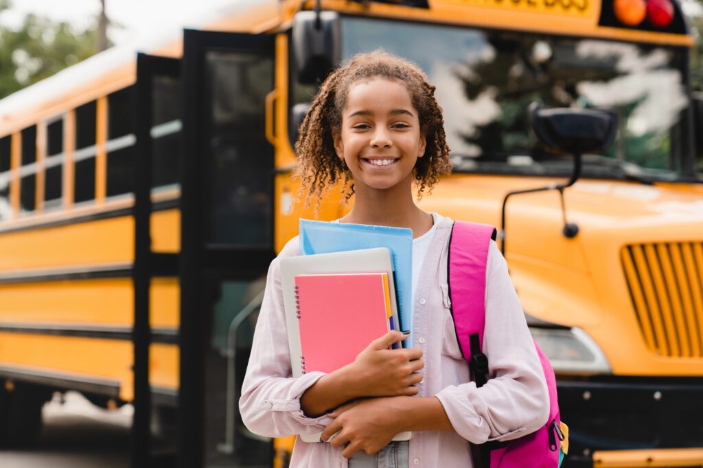 Smiling african-american schoolgirl going back to school with books and copybooks