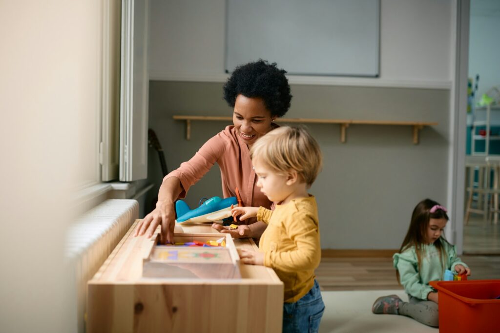 Joyeux professeur noir et petit garçon jouant avec des puzzles à la maternelle.